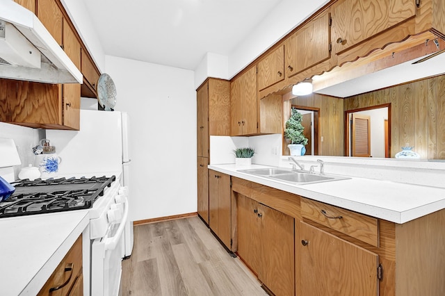 kitchen with light countertops, light wood-style flooring, a sink, gas range, and under cabinet range hood