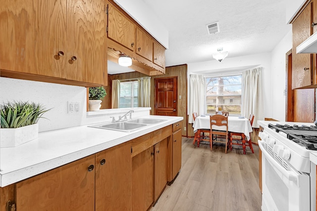 kitchen featuring brown cabinets, white gas range, light countertops, a textured ceiling, and a sink