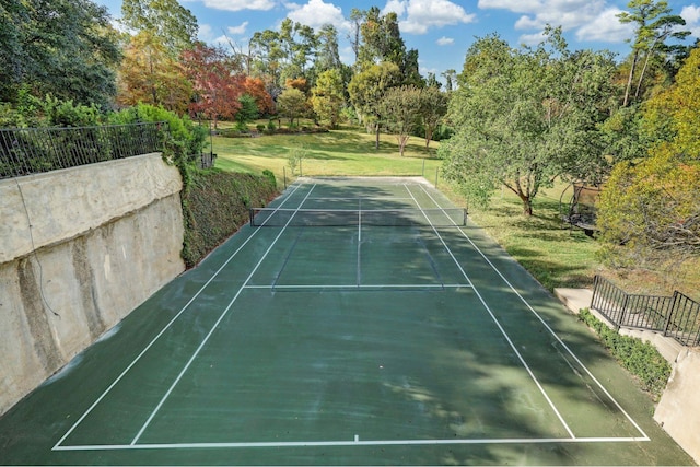 view of tennis court featuring a lawn and fence