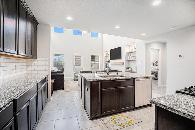 kitchen with open floor plan, stainless steel dishwasher, a sink, and light stone countertops