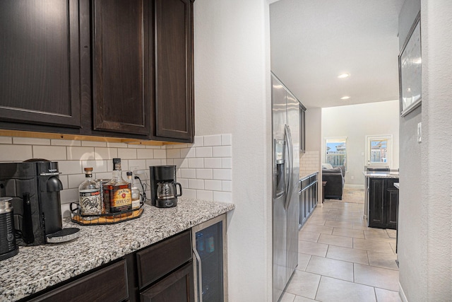 kitchen featuring light stone counters, wine cooler, tasteful backsplash, dark brown cabinets, and stainless steel fridge