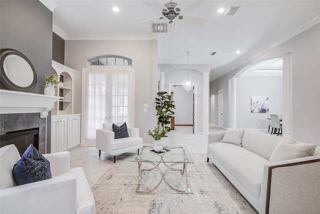 tiled living room with ceiling fan with notable chandelier, ornamental molding, a premium fireplace, and recessed lighting