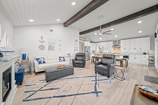 living area featuring light wood-type flooring, a glass covered fireplace, vaulted ceiling with beams, and recessed lighting