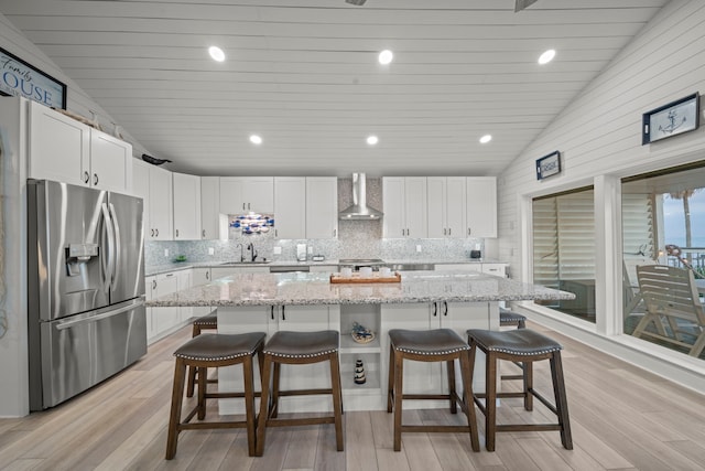 kitchen with white cabinets, stainless steel fridge with ice dispenser, lofted ceiling, wall chimney exhaust hood, and a sink