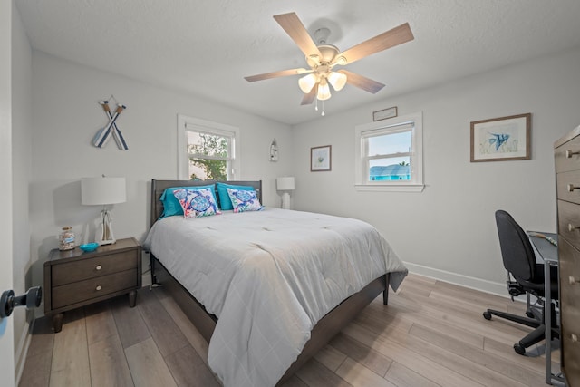 bedroom with ceiling fan, a textured ceiling, baseboards, and wood finished floors