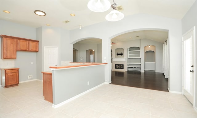 kitchen featuring built in shelves, brown cabinetry, light countertops, light tile patterned floors, and lofted ceiling