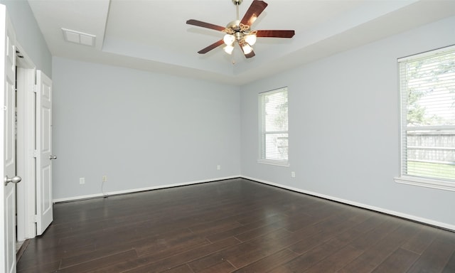 empty room with a wealth of natural light, dark wood finished floors, and a tray ceiling