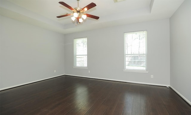 unfurnished room with a wealth of natural light, a tray ceiling, and dark wood-style flooring