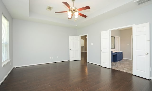 interior space with visible vents, a raised ceiling, wood finished floors, and a ceiling fan