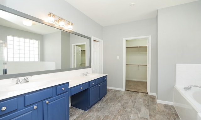 full bathroom with a walk in closet, wood finish floors, double vanity, a bath, and a sink