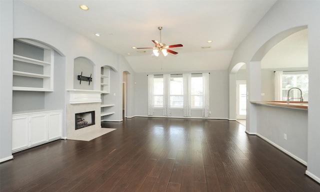 unfurnished living room featuring built in shelves, plenty of natural light, ceiling fan, and wood finished floors