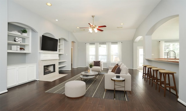 living area featuring built in shelves, plenty of natural light, wood finished floors, and a fireplace with flush hearth