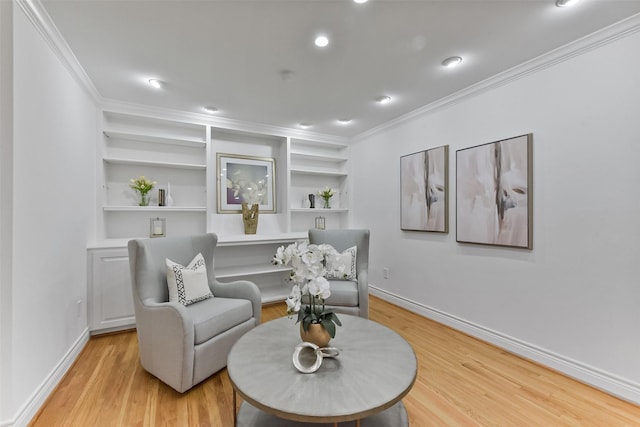 sitting room featuring baseboards, light wood-style floors, built in shelves, and crown molding