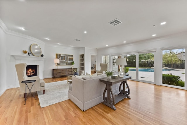 living area featuring visible vents, a warm lit fireplace, light wood-type flooring, and ornamental molding