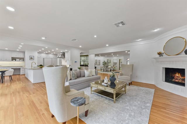 living room with visible vents, light wood-style flooring, a fireplace, recessed lighting, and crown molding