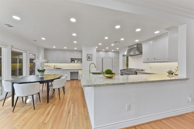 kitchen with a sink, light wood-type flooring, recessed lighting, wall chimney exhaust hood, and range