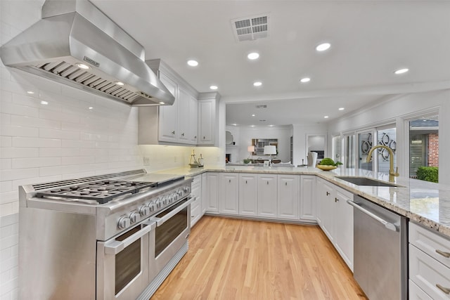 kitchen featuring visible vents, light wood-style flooring, a sink, stainless steel appliances, and wall chimney exhaust hood