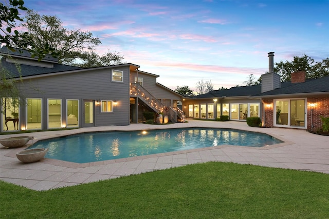 pool at dusk featuring a patio, stairway, a yard, and an outdoor pool