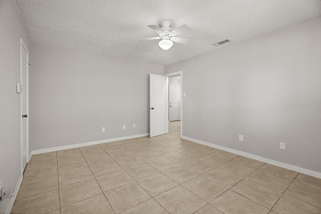 spare room with a textured ceiling, light tile patterned floors, visible vents, baseboards, and a ceiling fan