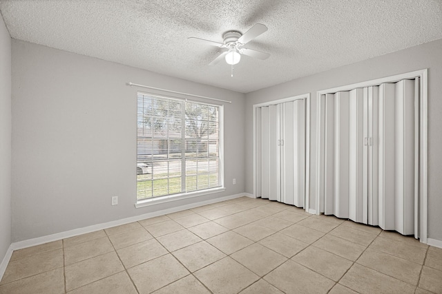 unfurnished bedroom featuring light tile patterned floors, a ceiling fan, baseboards, and two closets