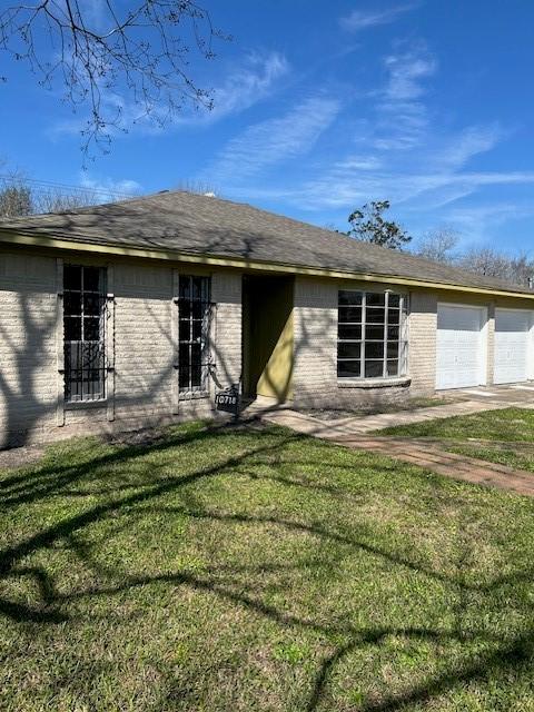 rear view of house with a garage, a yard, driveway, and brick siding