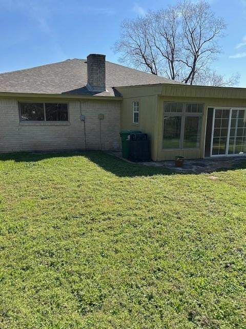 back of property with brick siding, a chimney, and a yard