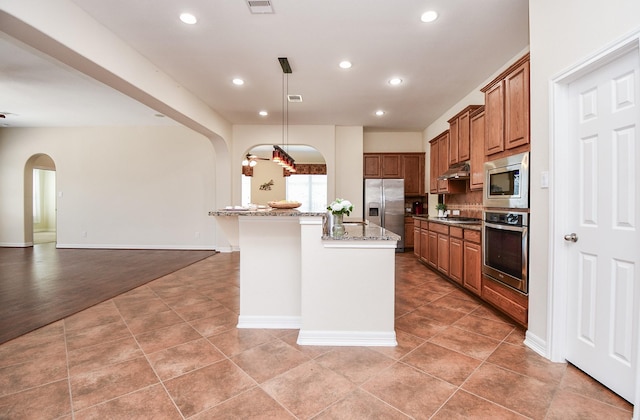 kitchen featuring arched walkways, appliances with stainless steel finishes, dark stone counters, and brown cabinets