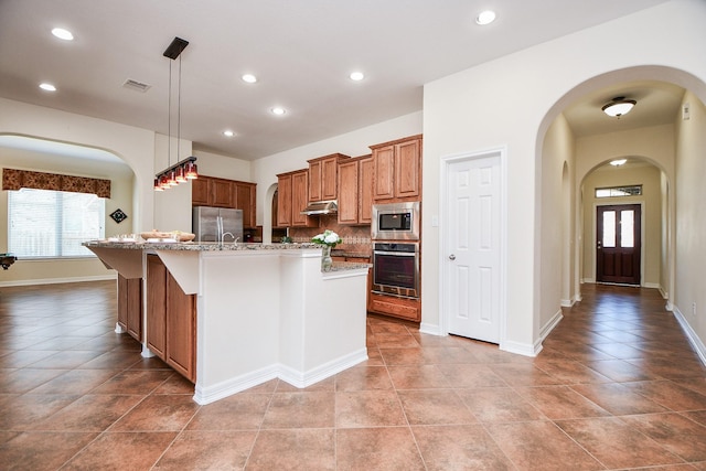 kitchen with under cabinet range hood, stainless steel appliances, visible vents, a wealth of natural light, and brown cabinetry