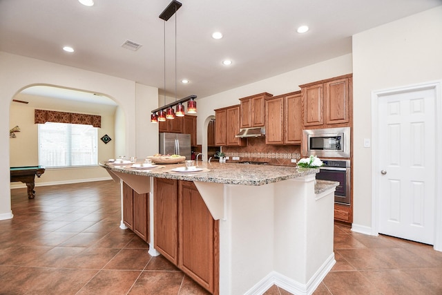 kitchen featuring tasteful backsplash, visible vents, brown cabinetry, stainless steel appliances, and under cabinet range hood