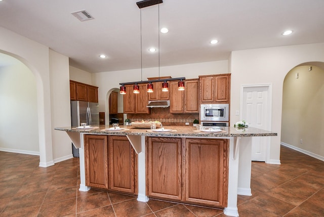 kitchen featuring arched walkways, under cabinet range hood, stainless steel appliances, visible vents, and backsplash