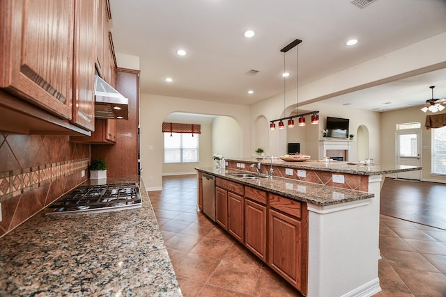 kitchen with range hood, stainless steel appliances, backsplash, open floor plan, and a sink