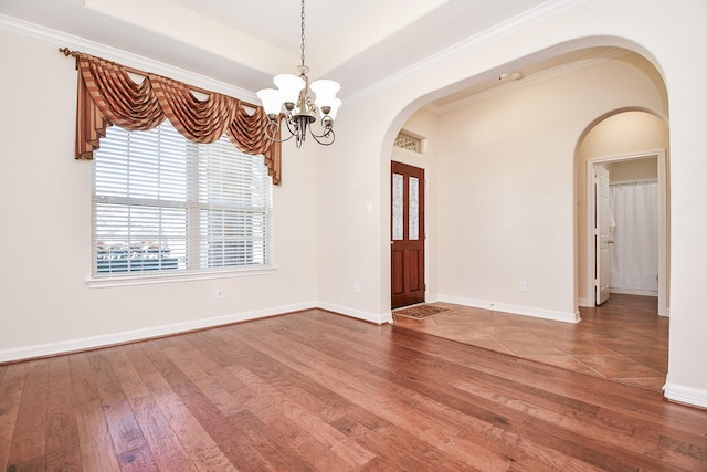 empty room featuring baseboards, arched walkways, a raised ceiling, hardwood / wood-style flooring, and a chandelier