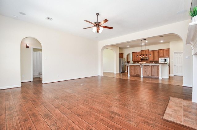 unfurnished living room with arched walkways, visible vents, dark wood finished floors, and ceiling fan