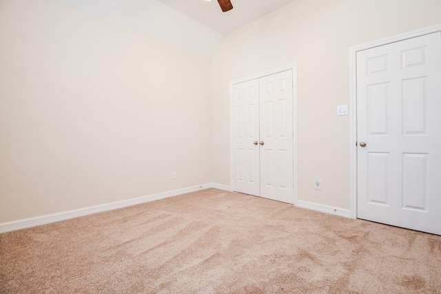 unfurnished bedroom featuring light carpet, baseboards, lofted ceiling, ceiling fan, and a closet