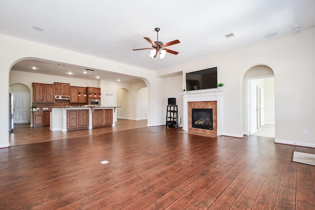 unfurnished living room with ceiling fan, dark wood-style flooring, a fireplace, visible vents, and baseboards