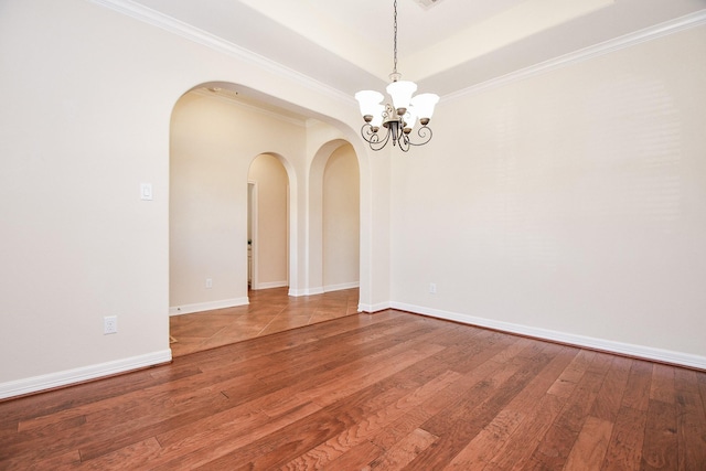 empty room featuring arched walkways, hardwood / wood-style floors, a notable chandelier, and baseboards