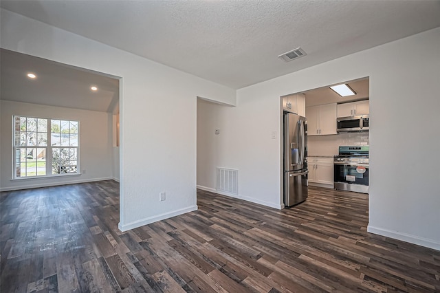 unfurnished living room featuring dark wood-style flooring, visible vents, and baseboards