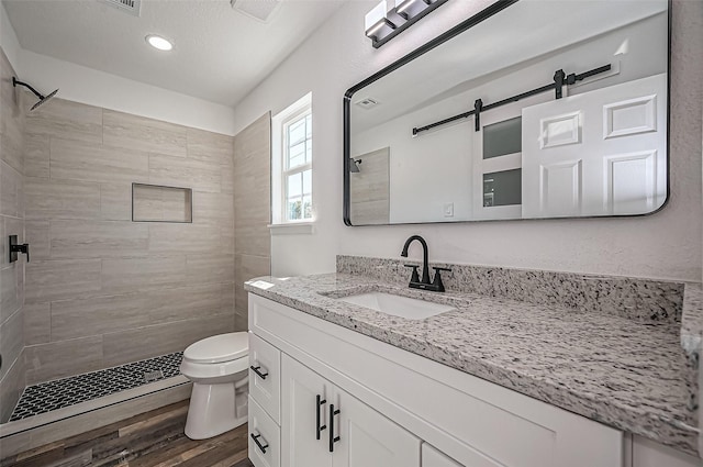 bathroom with tiled shower, wood finished floors, and toilet