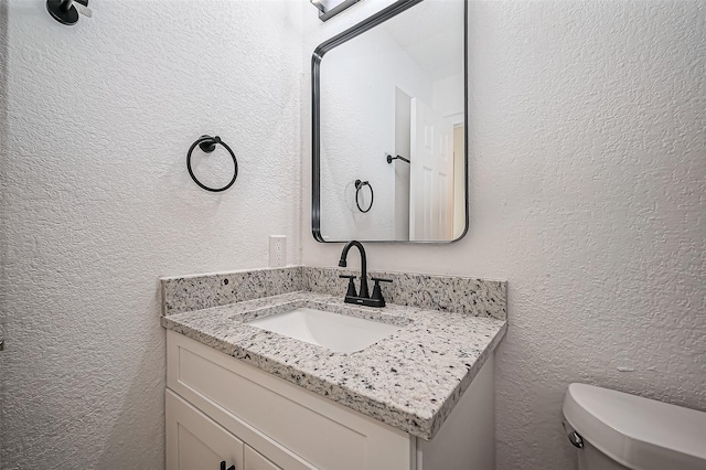 half bathroom with a textured wall, vanity, and toilet