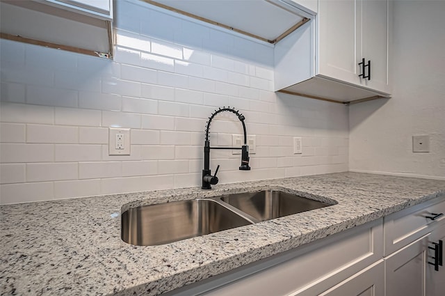 kitchen featuring tasteful backsplash, light stone counters, white cabinets, and a sink