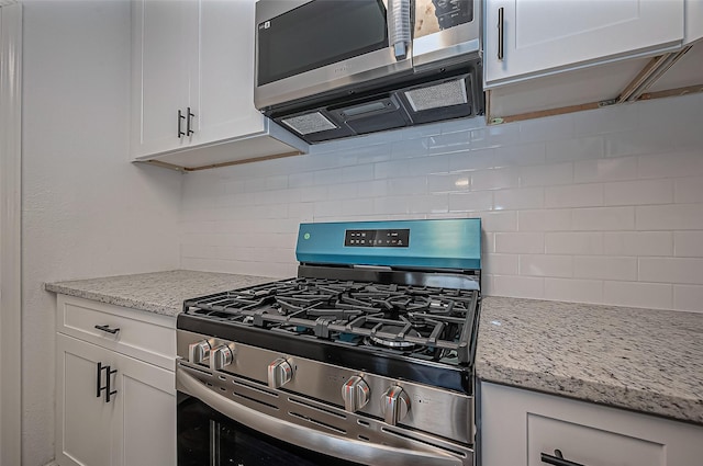 kitchen featuring stainless steel appliances, white cabinets, decorative backsplash, and light stone countertops