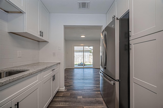 kitchen with visible vents, backsplash, freestanding refrigerator, white cabinetry, and light stone countertops