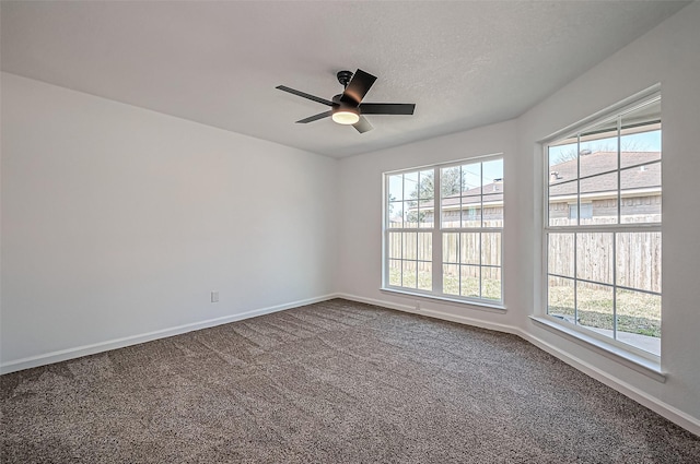 empty room featuring a ceiling fan, dark colored carpet, a textured ceiling, and baseboards