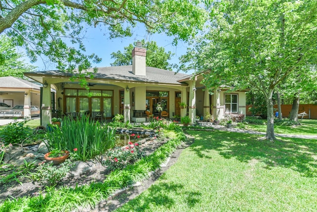 rear view of house with stucco siding, a chimney, and a yard