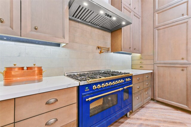 kitchen featuring light stone countertops, wall chimney range hood, range with two ovens, and backsplash