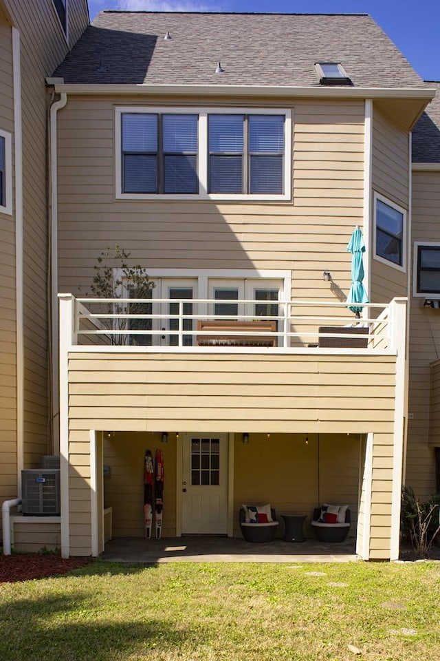 back of house with roof with shingles, central AC unit, and a lawn