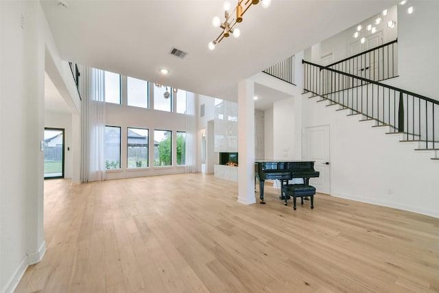 living room featuring a warm lit fireplace, visible vents, light wood finished floors, and stairs