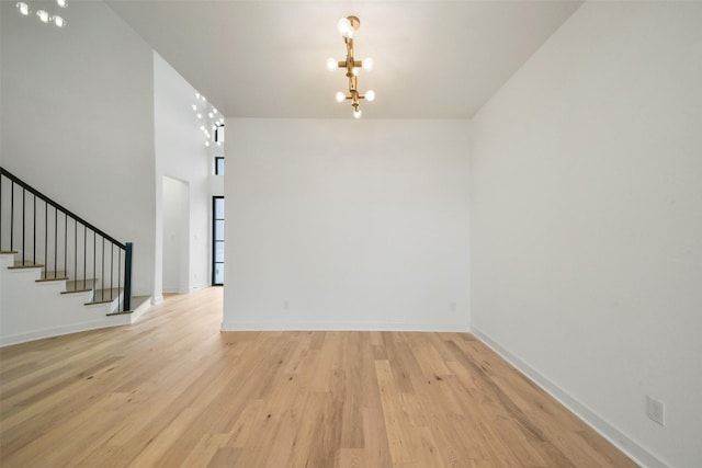 spare room with stairs, light wood-type flooring, a chandelier, and baseboards