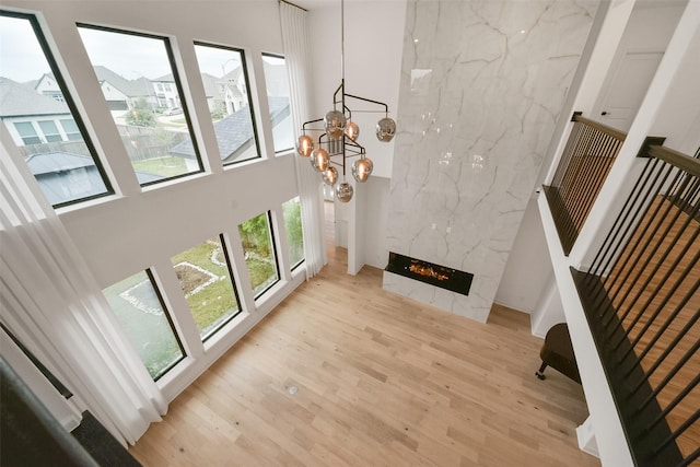 unfurnished living room featuring a chandelier, a premium fireplace, light wood-type flooring, and a towering ceiling