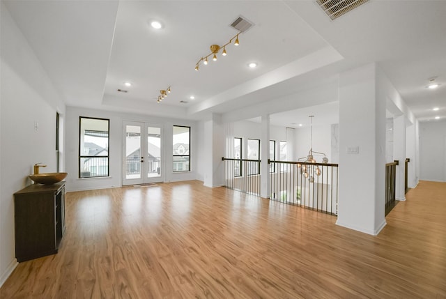 empty room with light wood finished floors, plenty of natural light, visible vents, and a raised ceiling